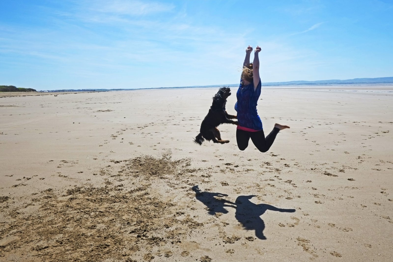 Woman jumping in air with dog on beach